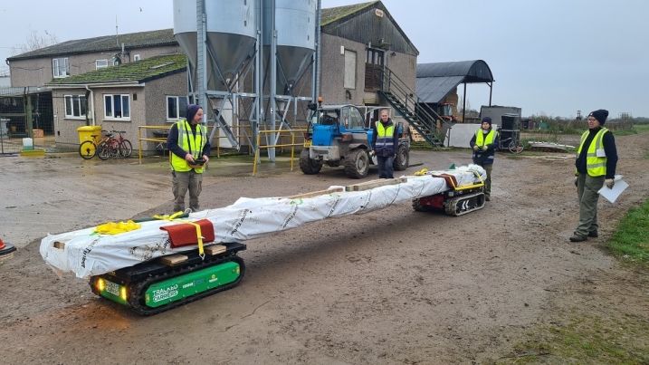 Roof beams on two robots, with four people stood by in high viz jackets.